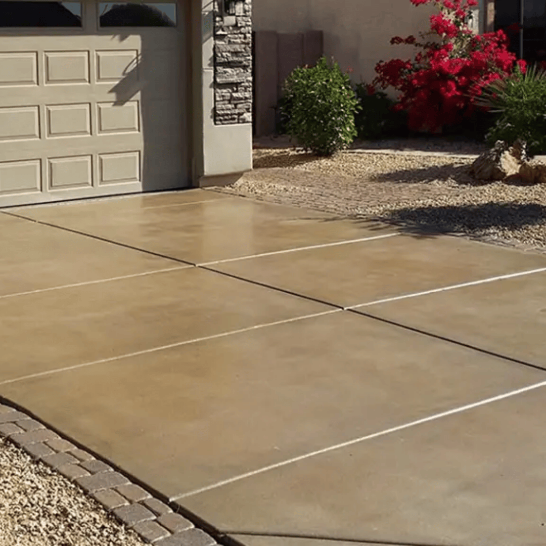 Beige concrete driveway in front of a garage, with gravel and landscaping.