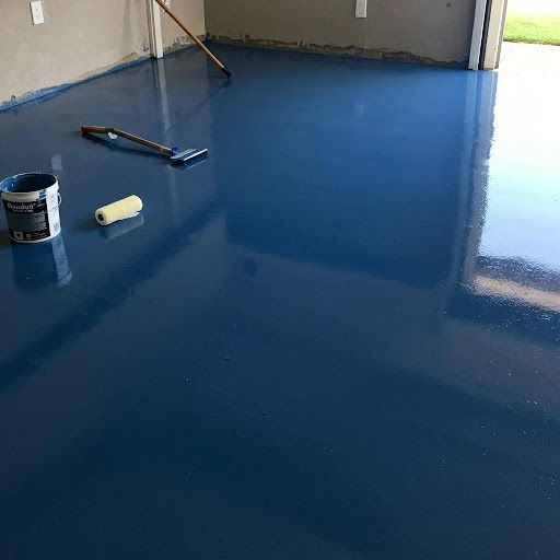 Blue epoxy-coated garage floor with tools and paint can, reflecting the light.