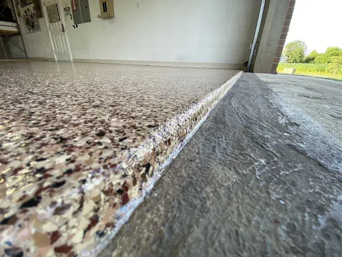 Close-up of a garage floor. The left side is a speckled epoxy coating, and the right is plain concrete.