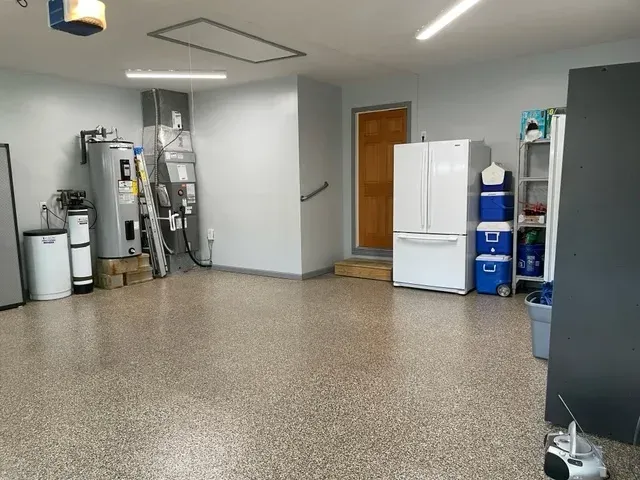 Spacious garage with epoxy floor, refrigerator, water heater, and a door.