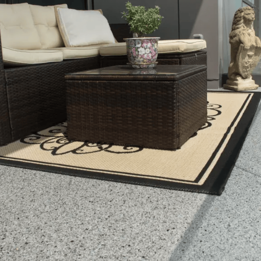 Outdoor seating area: wicker furniture, coffee table, floral rug, plant, and decorative statue.