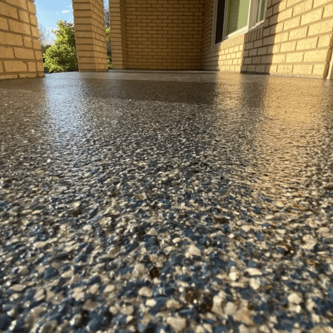 A close-up view of a wet, speckled, concrete porch floor beneath a brick structure.