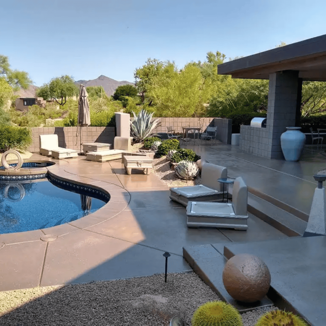 A patio with a pool, seating areas, and desert landscaping under a sunny sky.