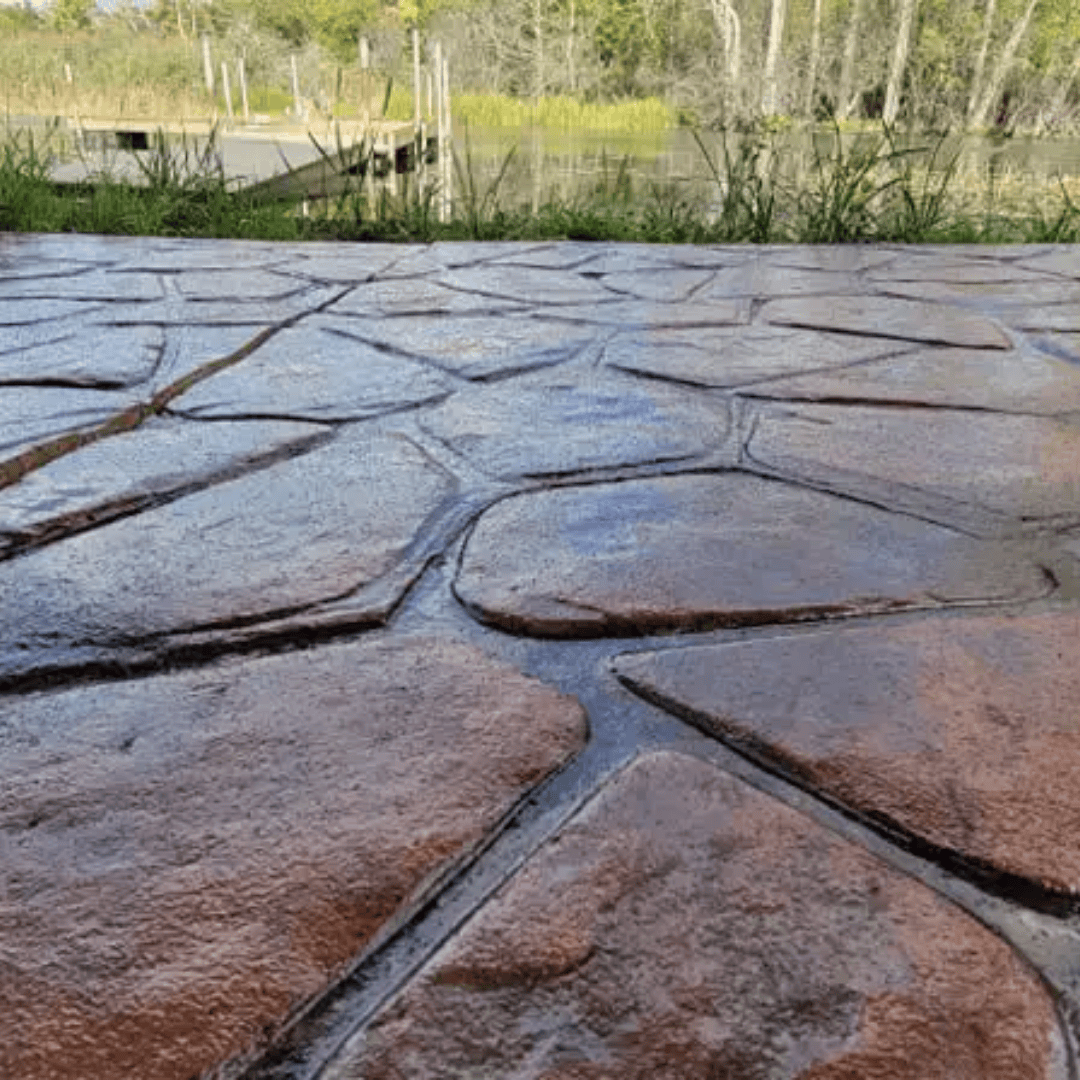Stone-textured concrete patio with a water view in the background. Brown and grey color scheme.