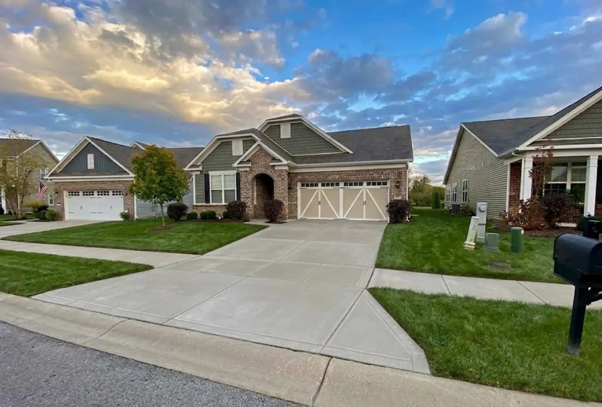 Two beige garage doors with glass windows, teal siding, gravel driveway.
