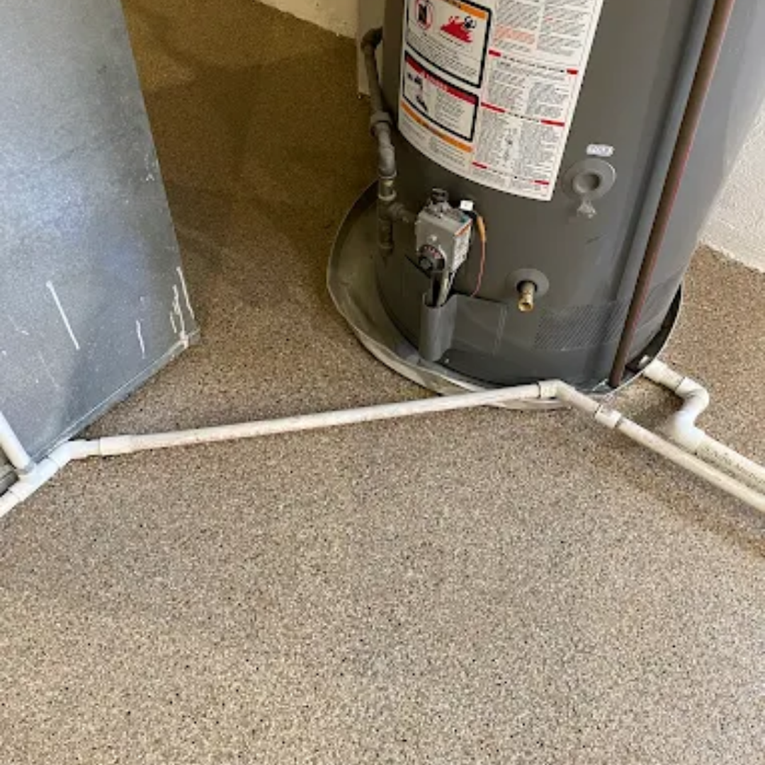Water heater with white pipes on a speckled floor next to a metal panel.