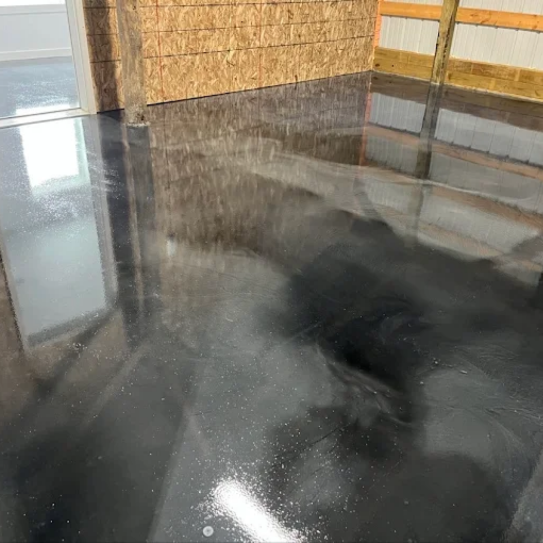 Shiny, dark gray epoxy floor in a building. Reflections from windows and walls are visible.