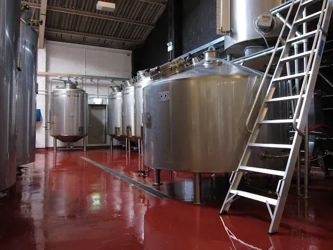 Brewery interior with stainless steel tanks, red floor, and metal ladder.