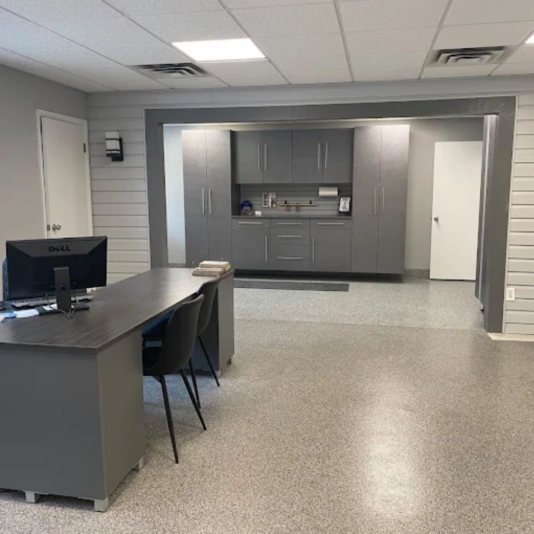 Office interior: Gray desk and cabinets, speckled floor, white door, and sink area.