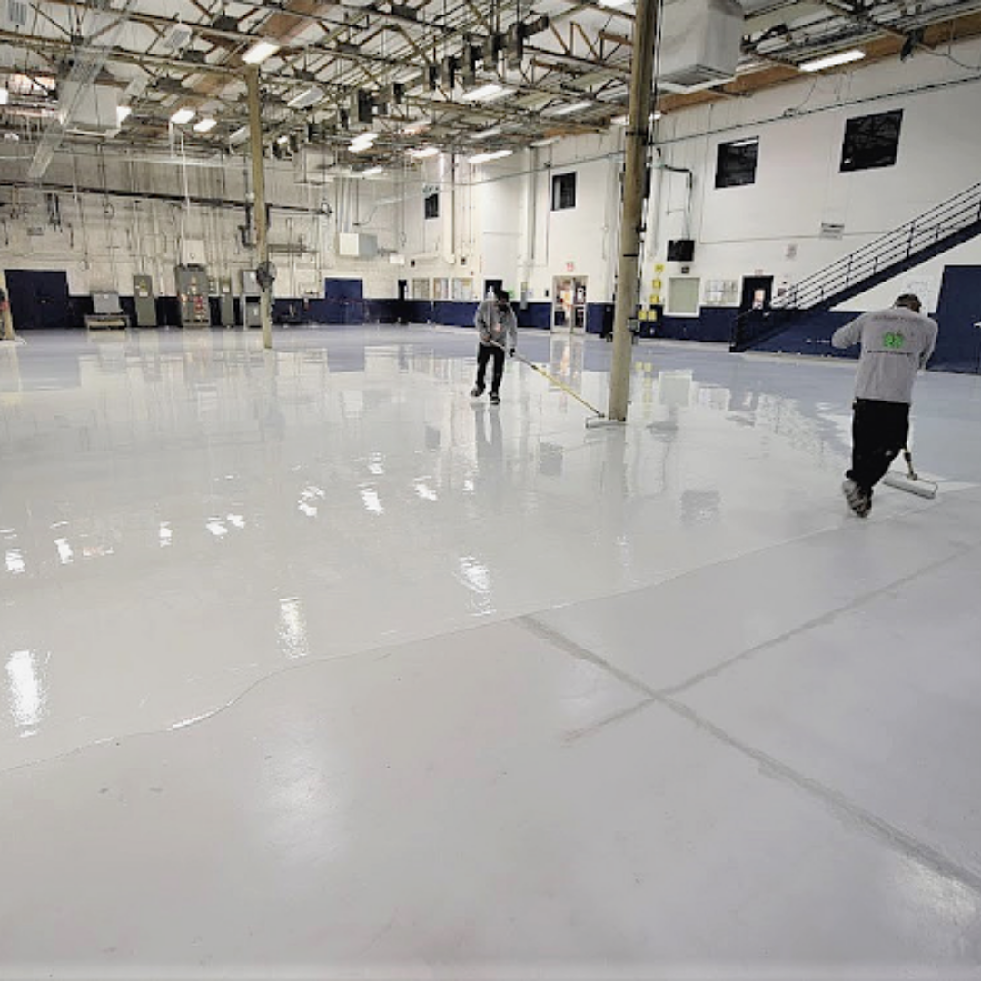 Two people applying white epoxy coating to a large warehouse floor.