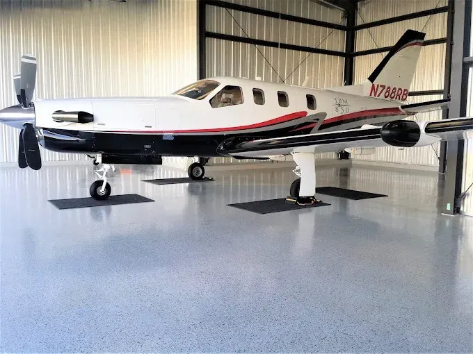 White and black airplane with red accents in a hangar, parked on a shiny gray floor.