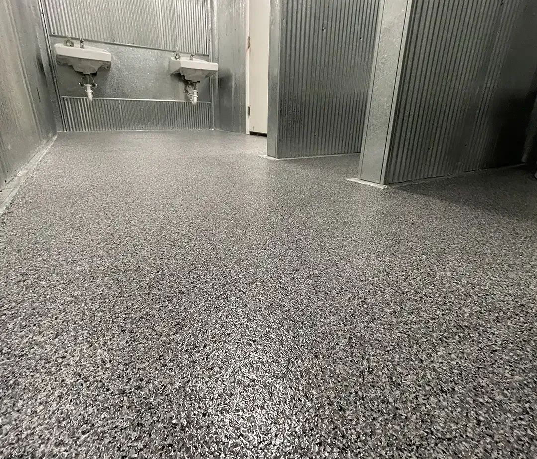 Bathroom with textured gray floors and corrugated metal walls. Two sinks are visible.