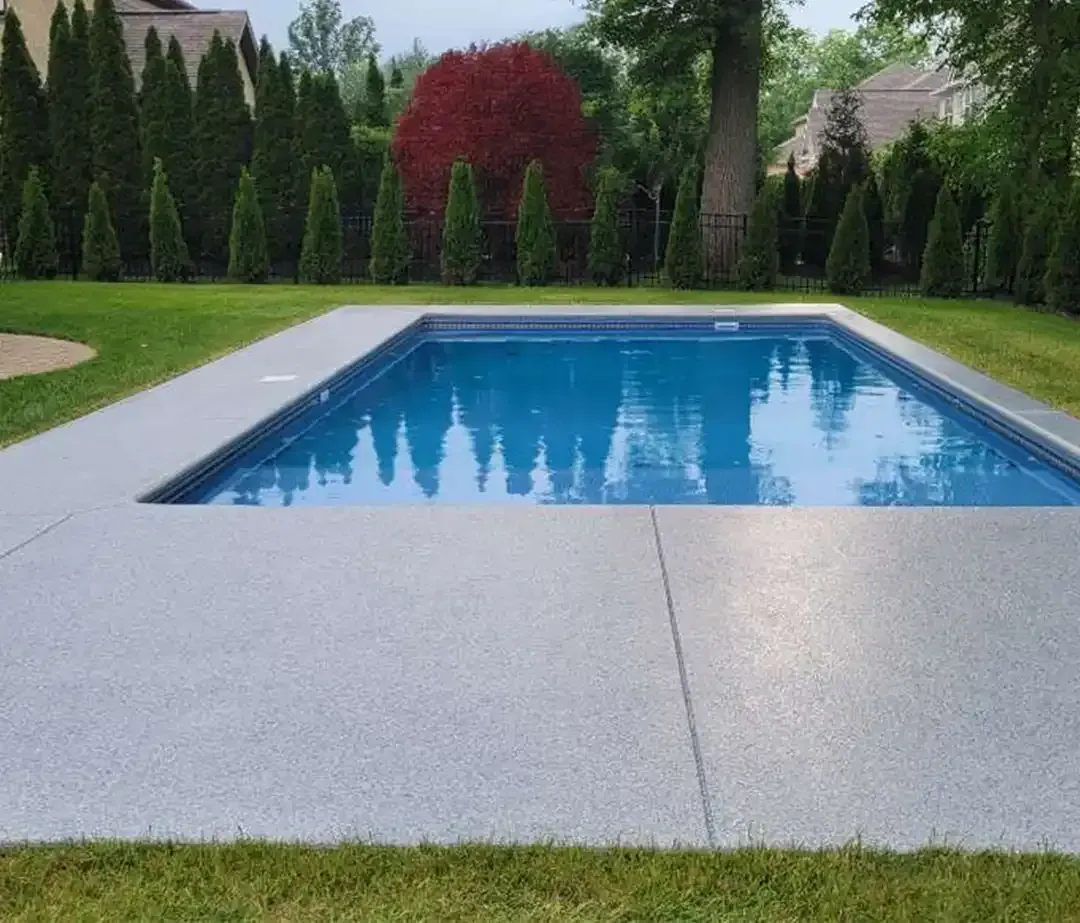Rectangular pool with gray concrete surround. Green grass and trees in background.