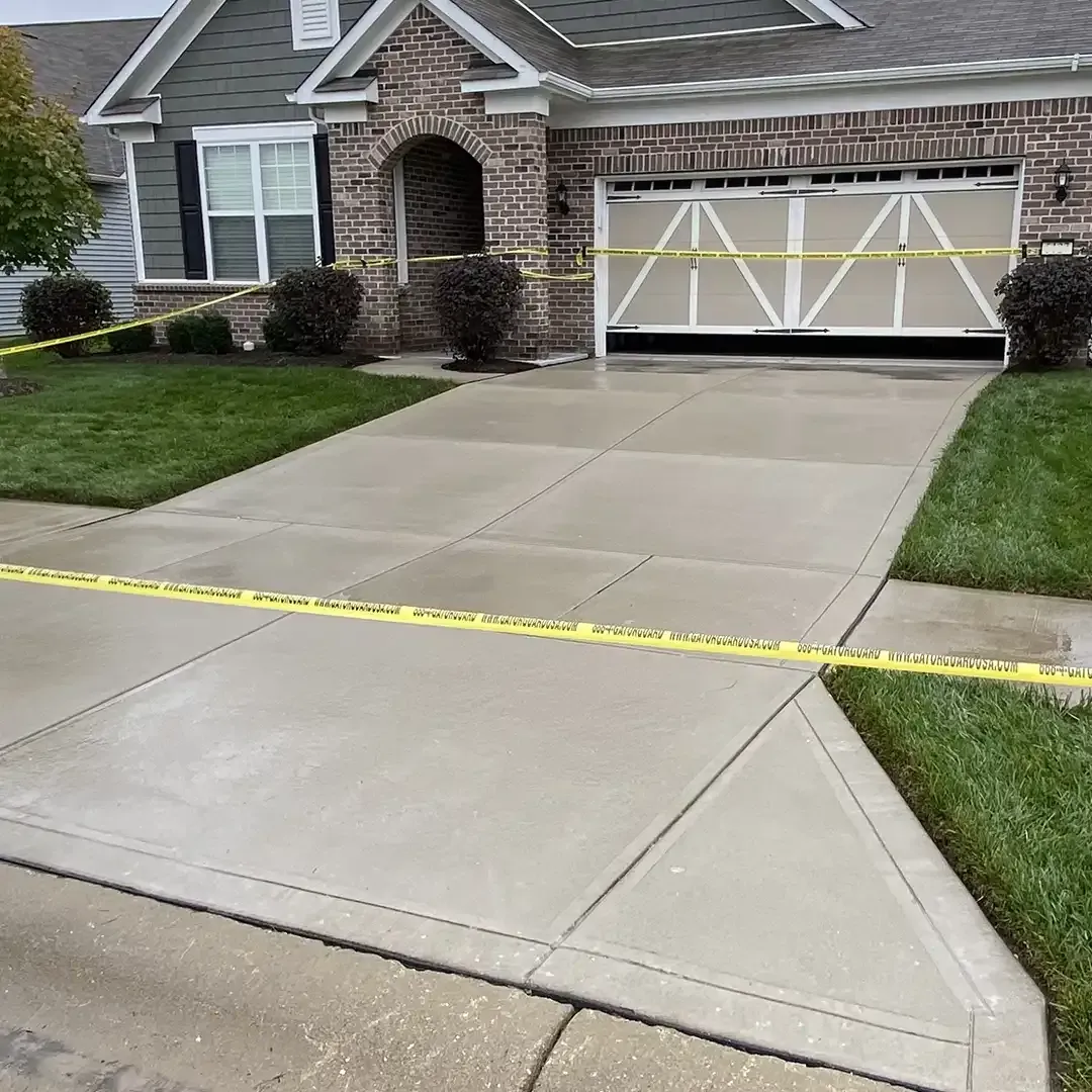 Freshly poured concrete driveway and walkway in front of a house, marked with yellow caution tape.