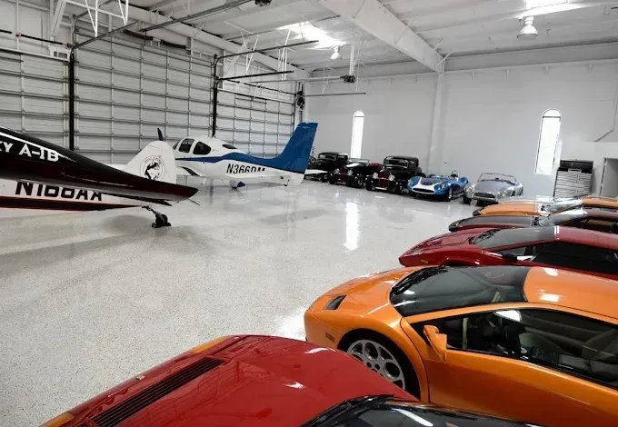 Large hangar with a private airplane, several luxury cars, and a glossy floor.