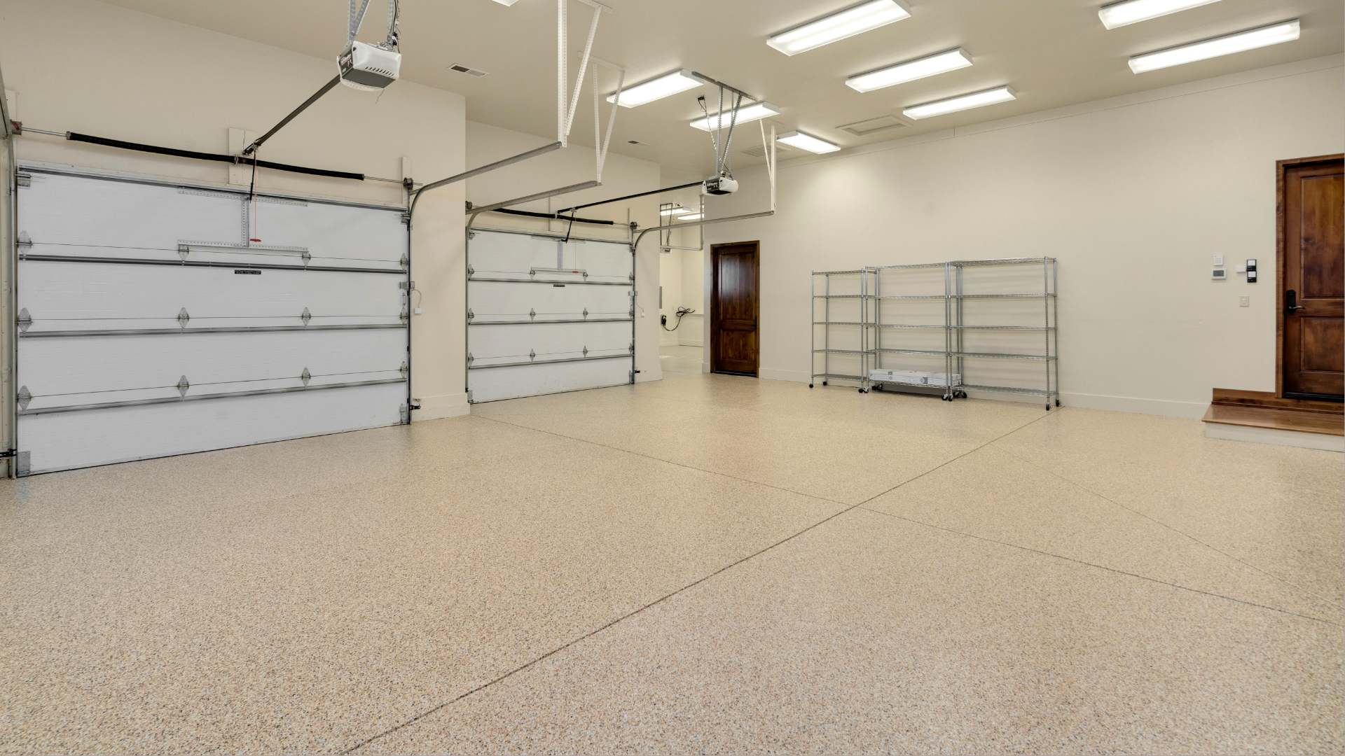 Empty, bright garage with white doors, speckled floor, metal shelving, and a wooden door.