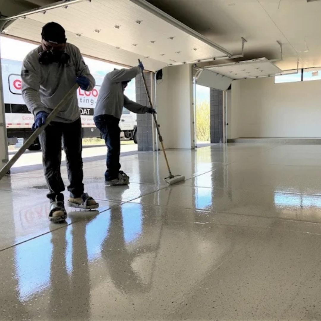 Two workers applying epoxy coating to a garage floor, with their reflections visible.
