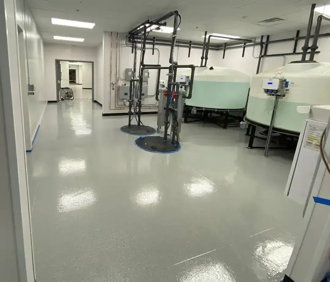 A clean industrial room with epoxy floors, tanks, and pipes. The room has a long hallway and bright lights.