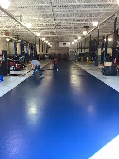 Man cleaning a bright blue shop floor in a large auto repair shop.