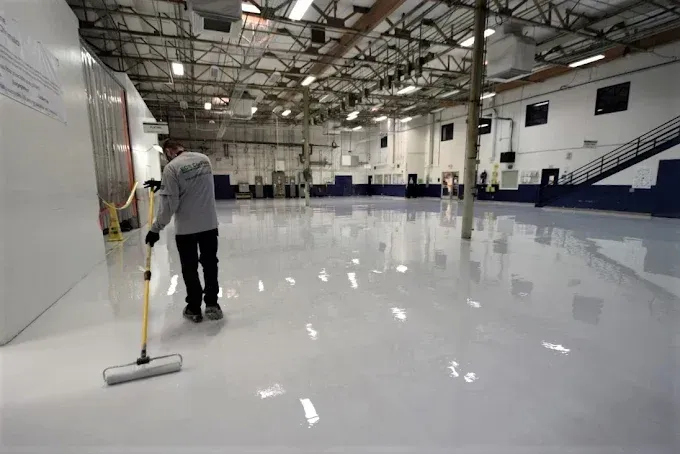 Person mopping a large, shiny, white floor in an industrial-looking building.