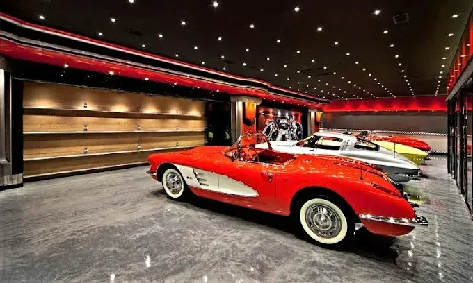 Red vintage convertible car parked in a luxury garage with other cars.