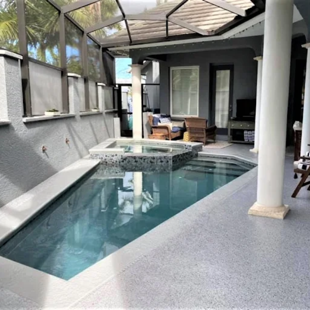 Indoor pool and jacuzzi, gray concrete, glass ceiling, white columns, sunny, outdoor furniture.