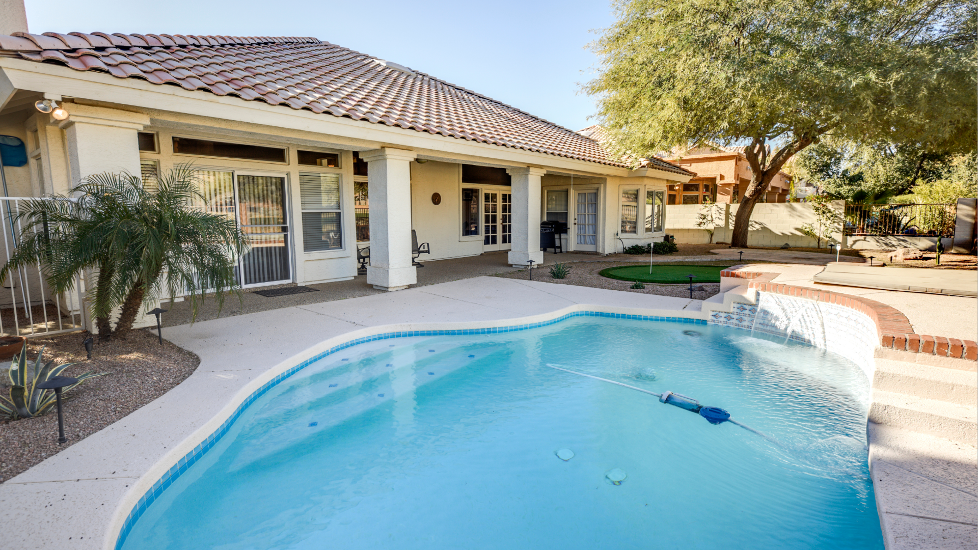 Backyard with a swimming pool, patio, and a house with a tile roof.