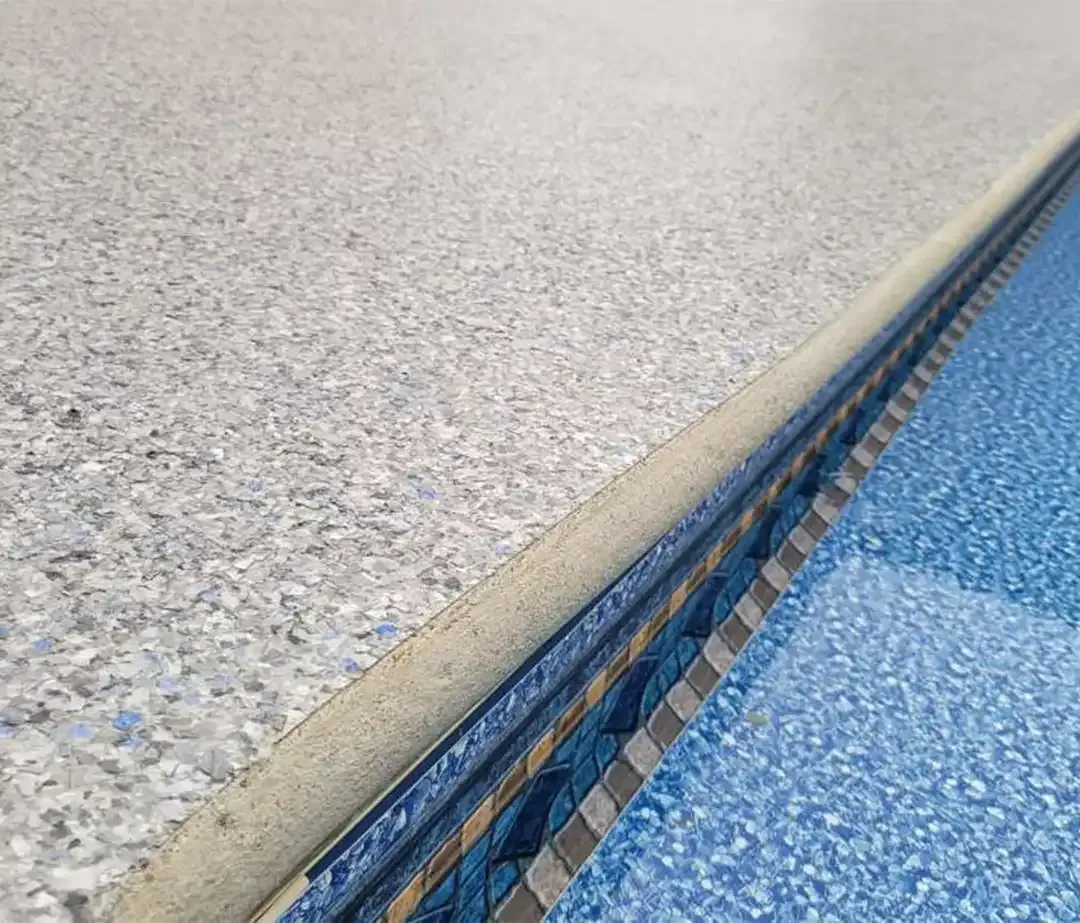 Close-up of a swimming pool edge with speckled concrete and blue water.