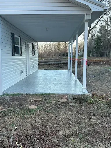 Covered porch with gray concrete floor, white posts, and white siding on a building.