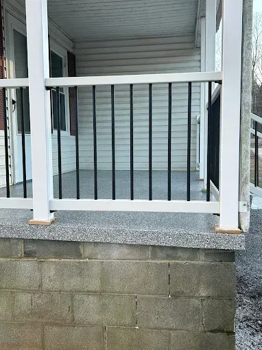 A porch with a white railing and black spindles, built on a cinder block foundation.