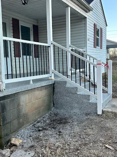 A house with a white porch, black railings, and gray concrete steps.