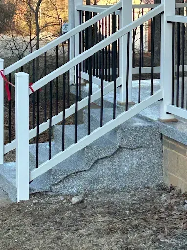 Outdoor concrete steps with black railing, white posts, and a crack.