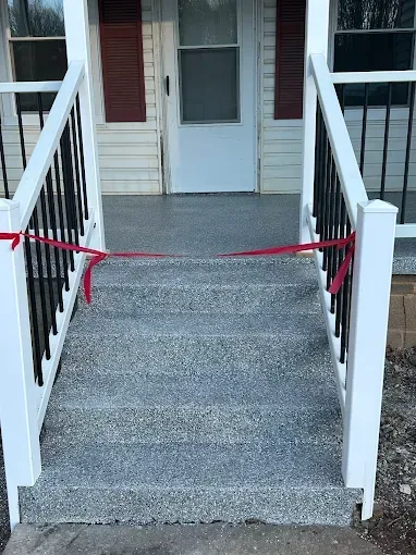 Grey concrete steps and porch with white railing, red ribbon closure.