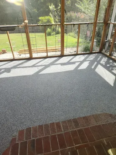 Gray speckled floor with sunlight and shadow from wooden frame structure. Brick steps lead into the room.