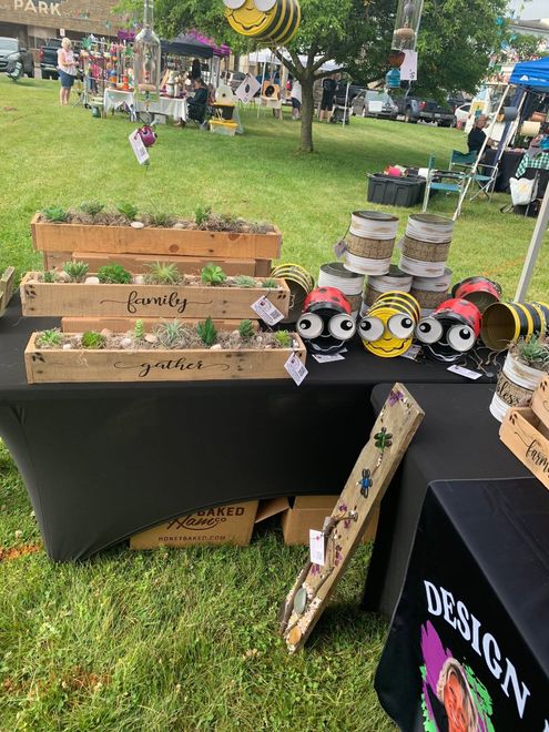 Outdoor craft market display with wooden planters and painted cat figurines on a black table.
