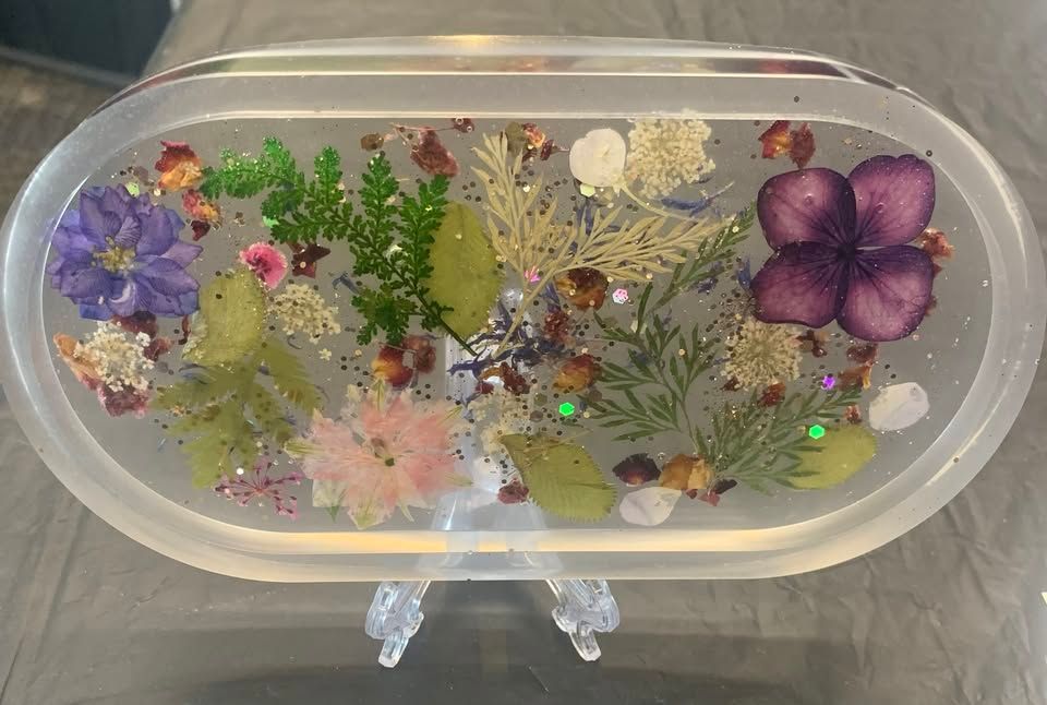 Clear plastic case with dried flowers, glitter, and purple floral decorations on a gray surface