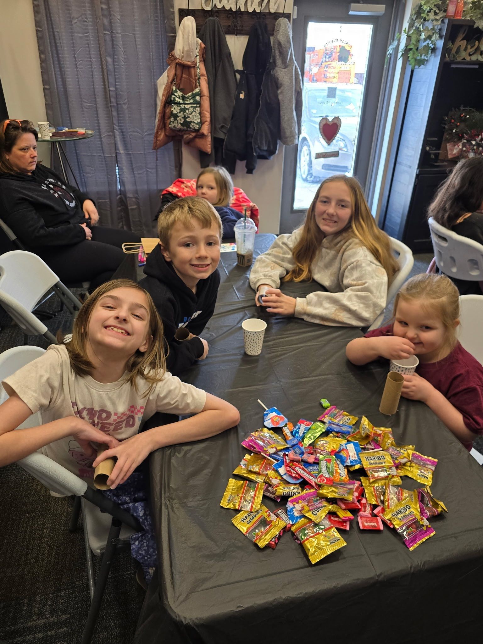 Children gathered around a table piled with wrapped candies in a cozy indoor setting