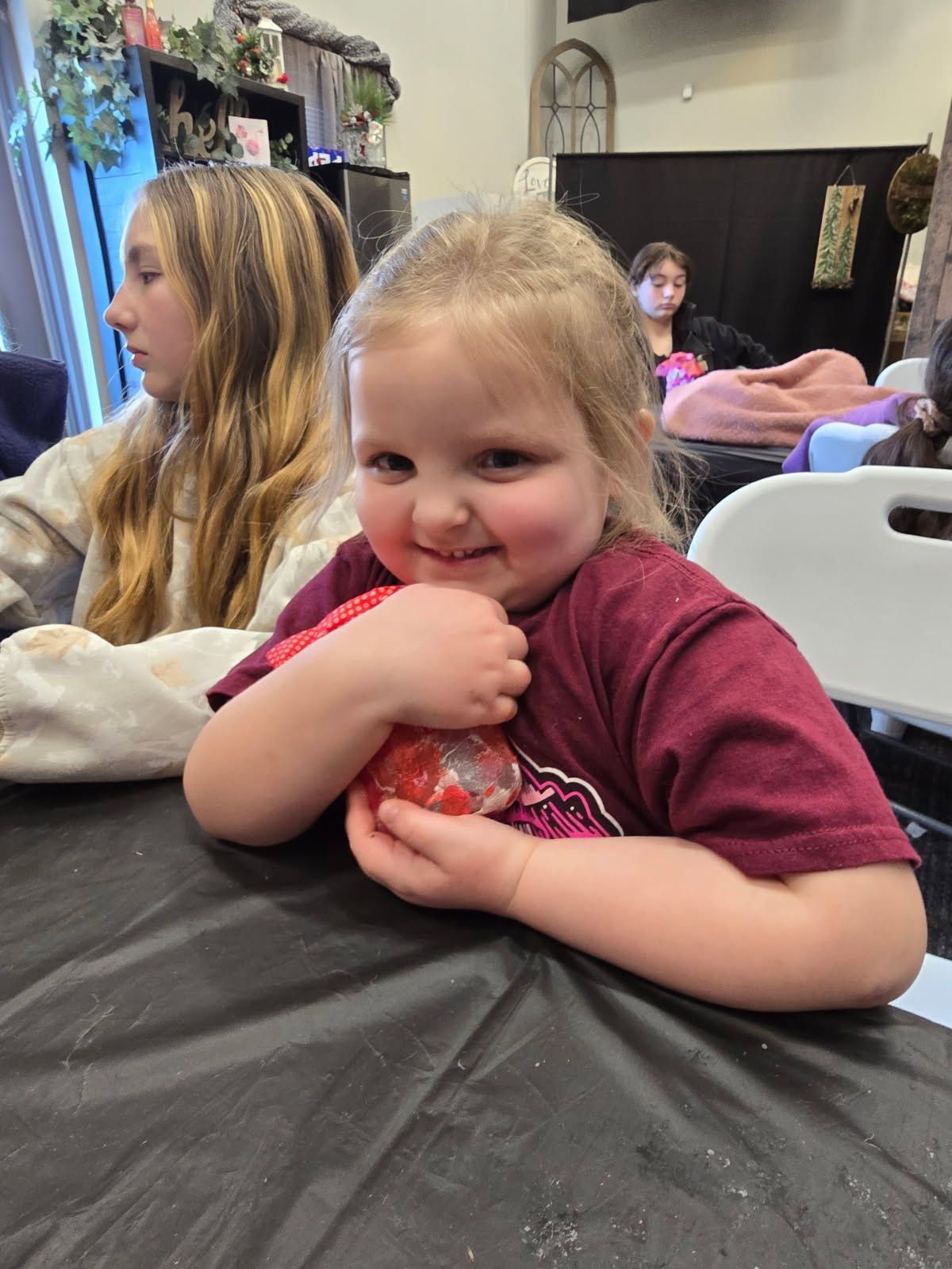 Smiling child in maroon shirt sitting at a table in a classroom or event space