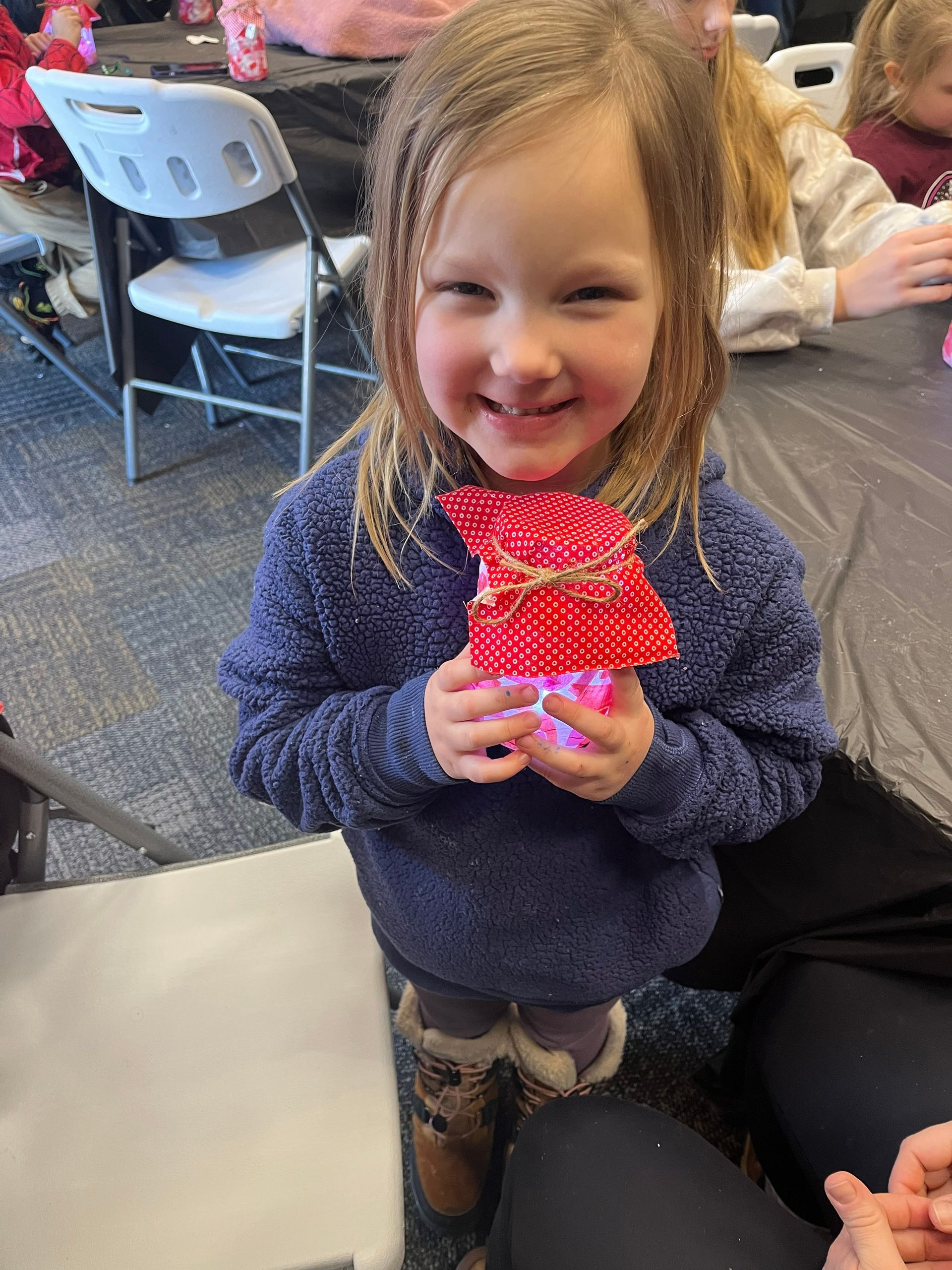 Smiling child holding a red polka-dot craft at a table in a casual indoor setting