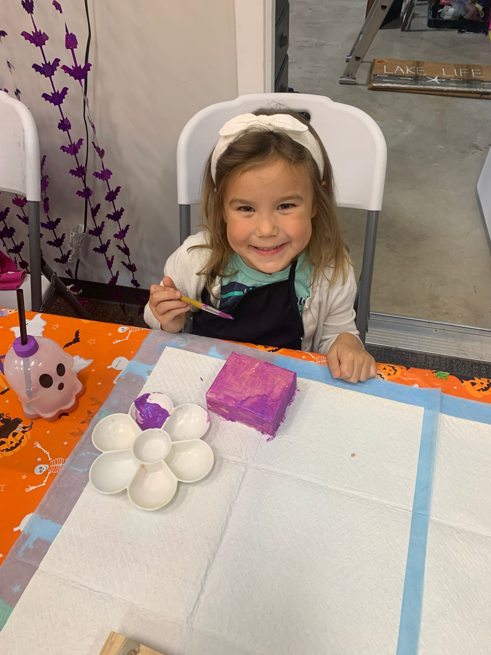 Smiling child at a craft table with white foam balls, a purple block, and a pumpkin decoration