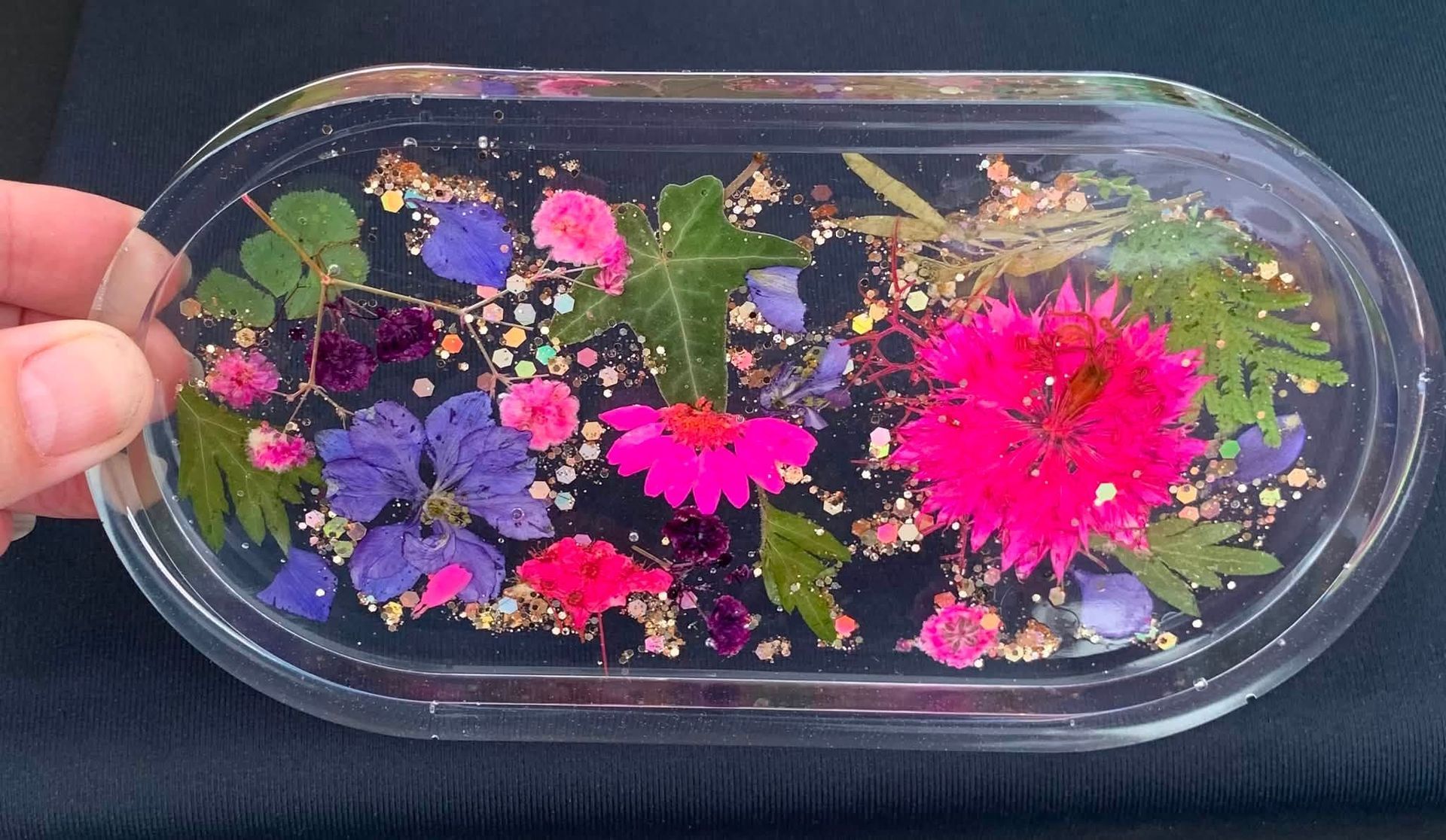 Hand holding a clear tray of floating colorful flowers and leaves in water