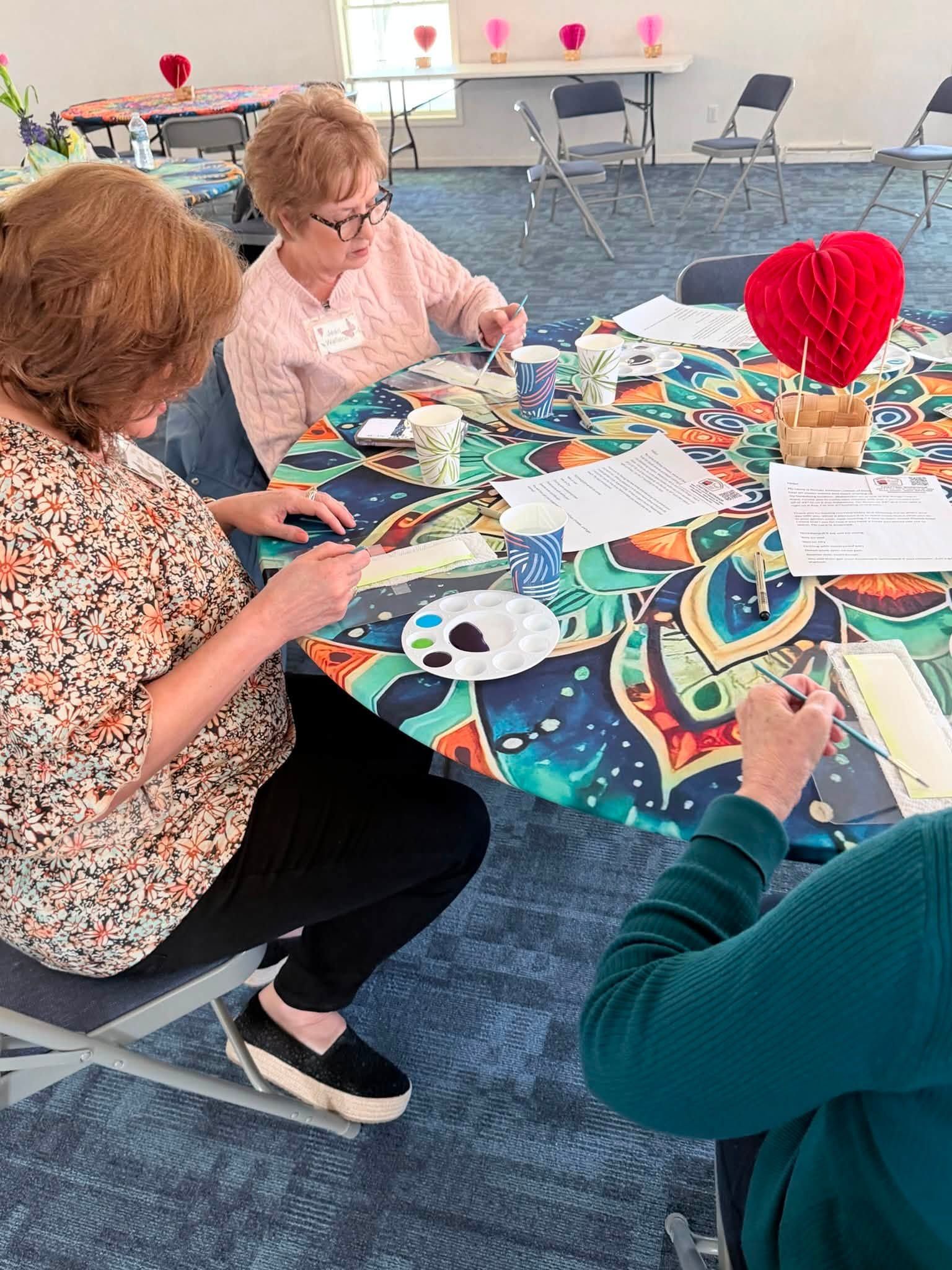 People crafting at a round table with colorful paper and supplies in a bright room