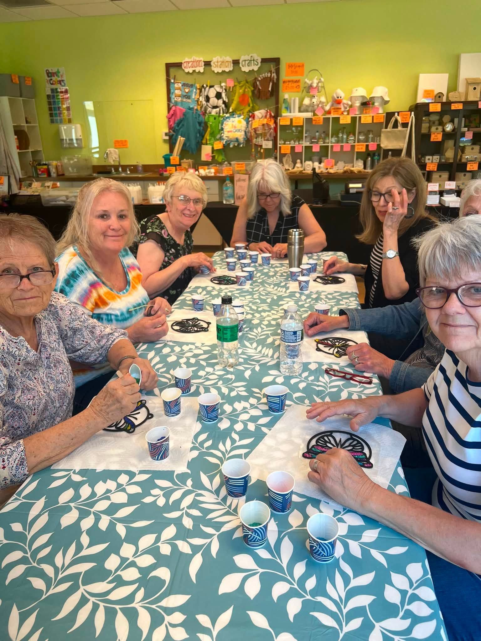 Group seated around a craft table, painting dice in a bright green room.