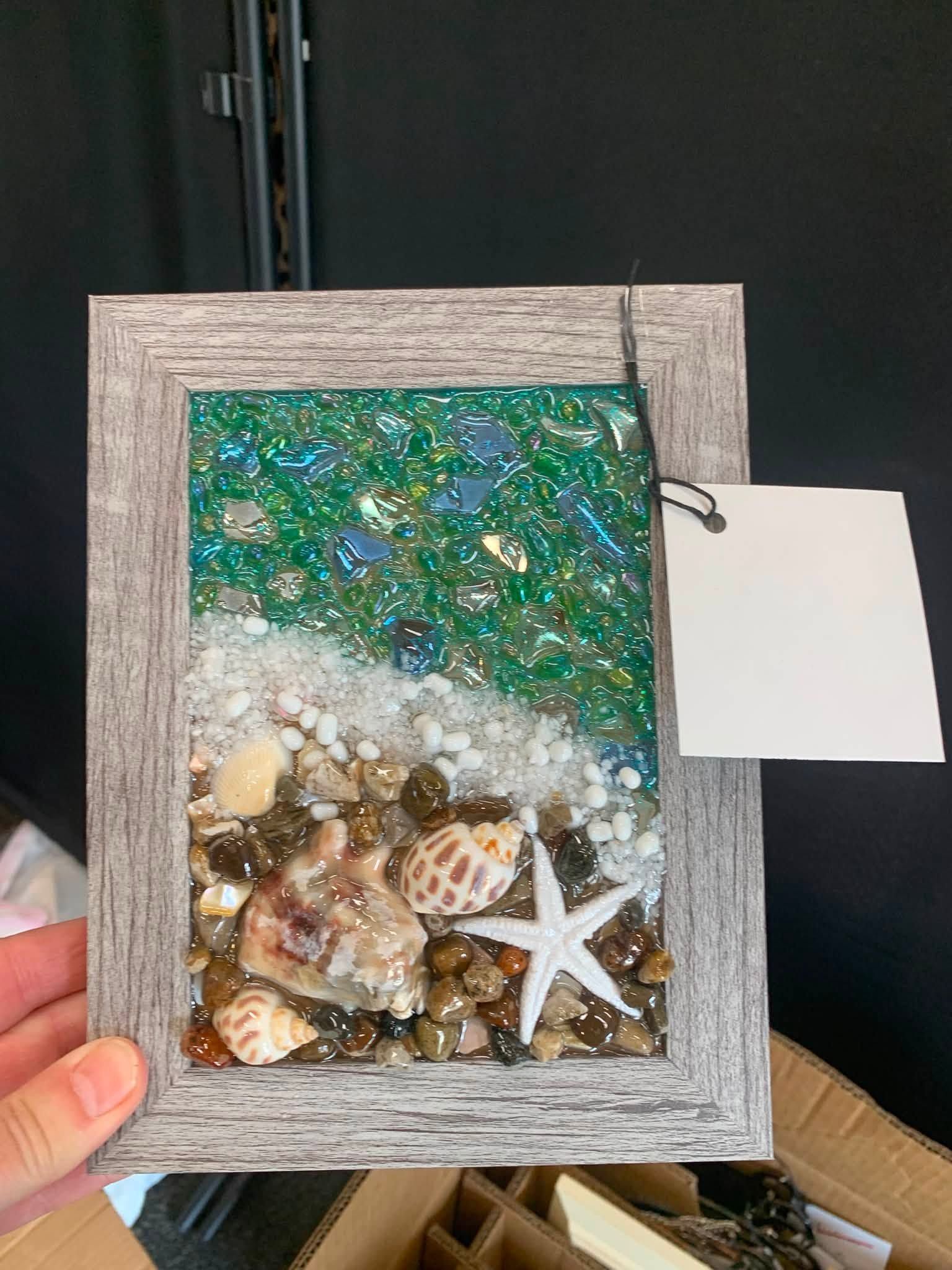 Small framed seashell and starfish display with green-blue glitter background, held in a hand