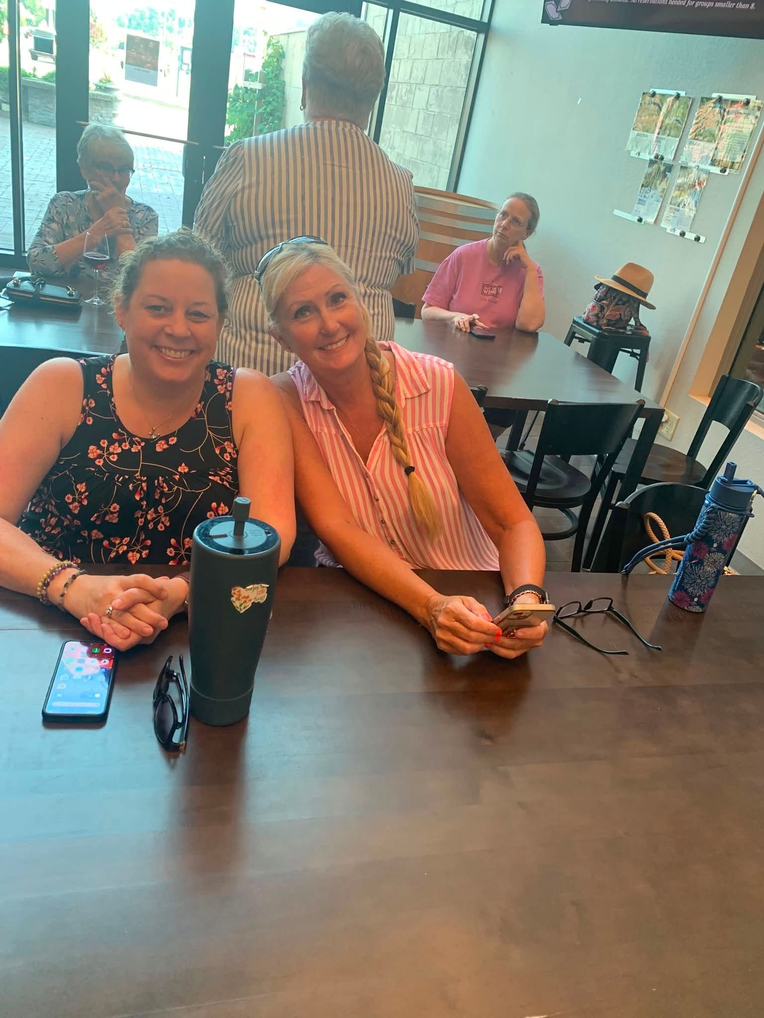 Two people smiling at a conference table with travel mugs in a bright office lounge