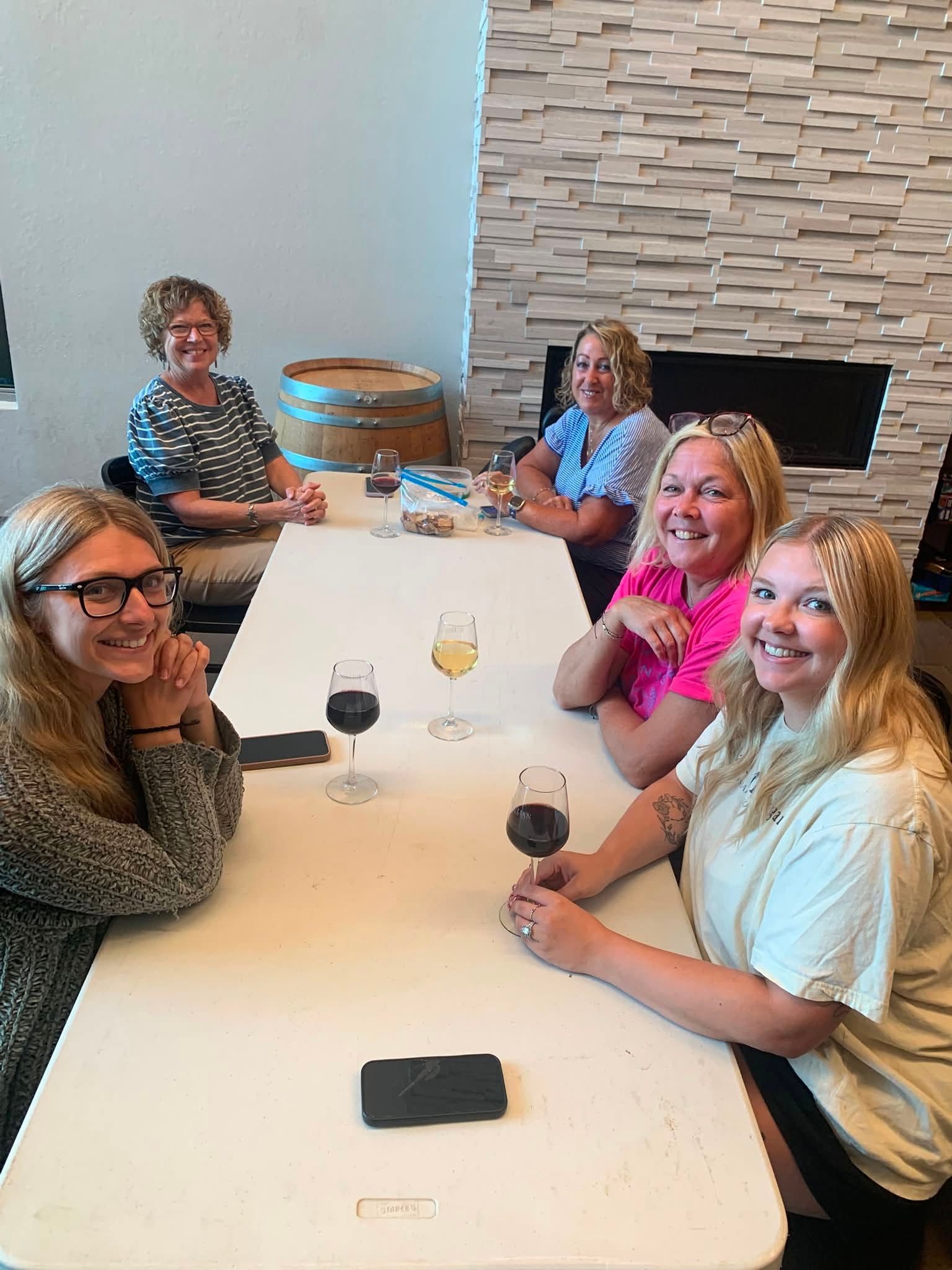 Five people seated around a white table in a bright dining room, smiling with drinks and a phone nearby