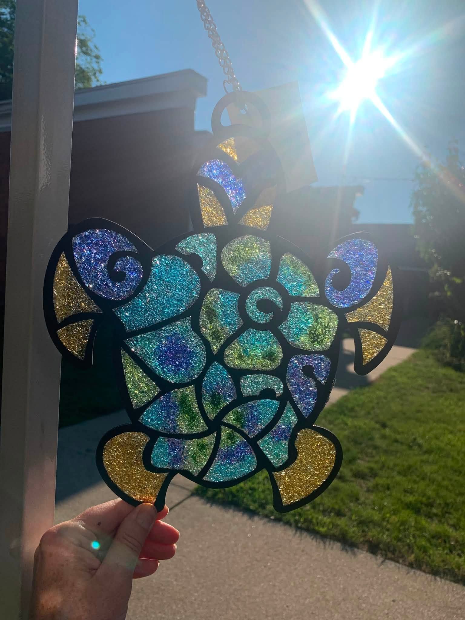 Handmade stained-glass sea turtle sun catcher held outdoors in bright sunlight