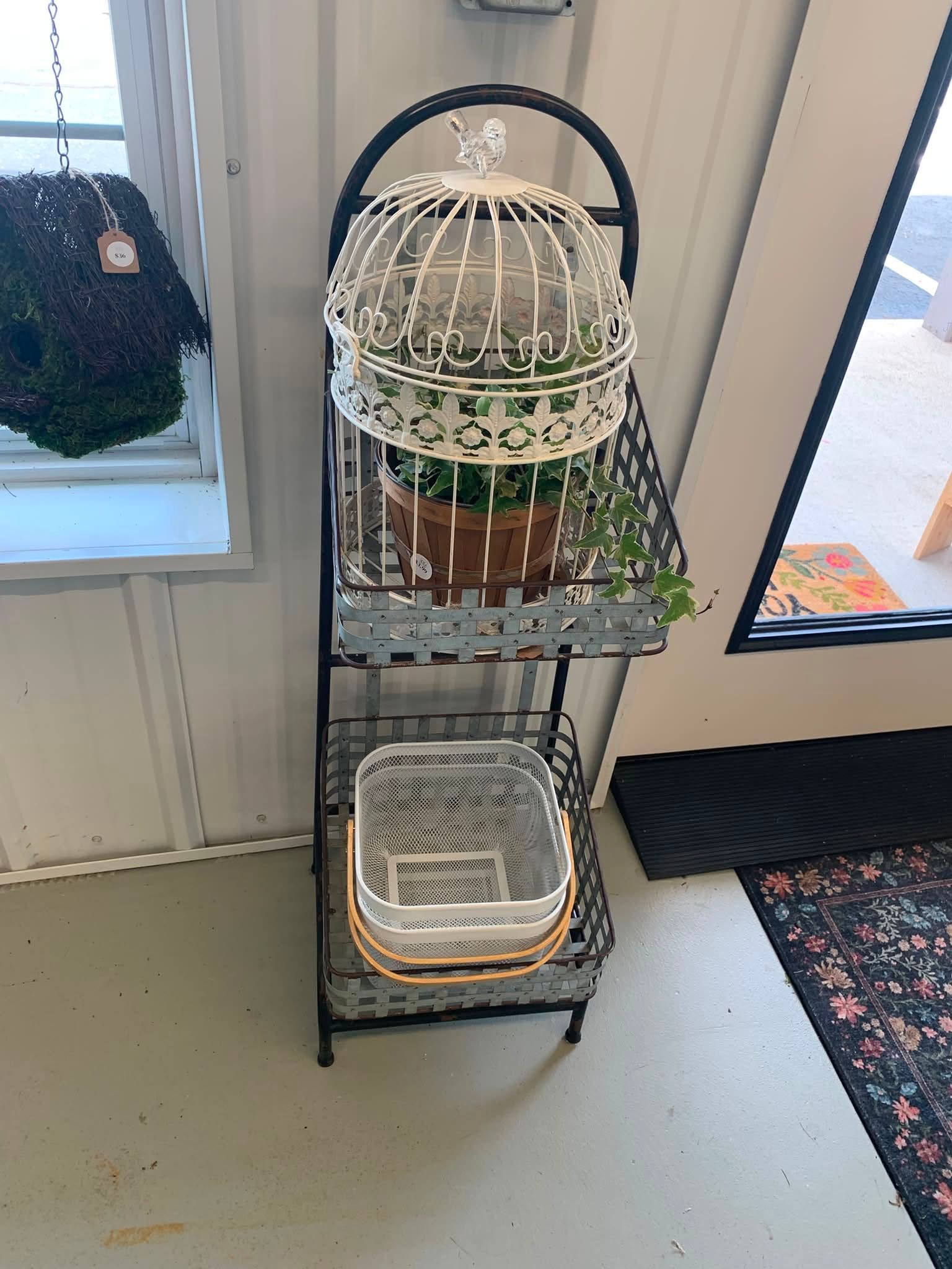 Black metal shelf with two bird cages and a potted plant near a window indoors