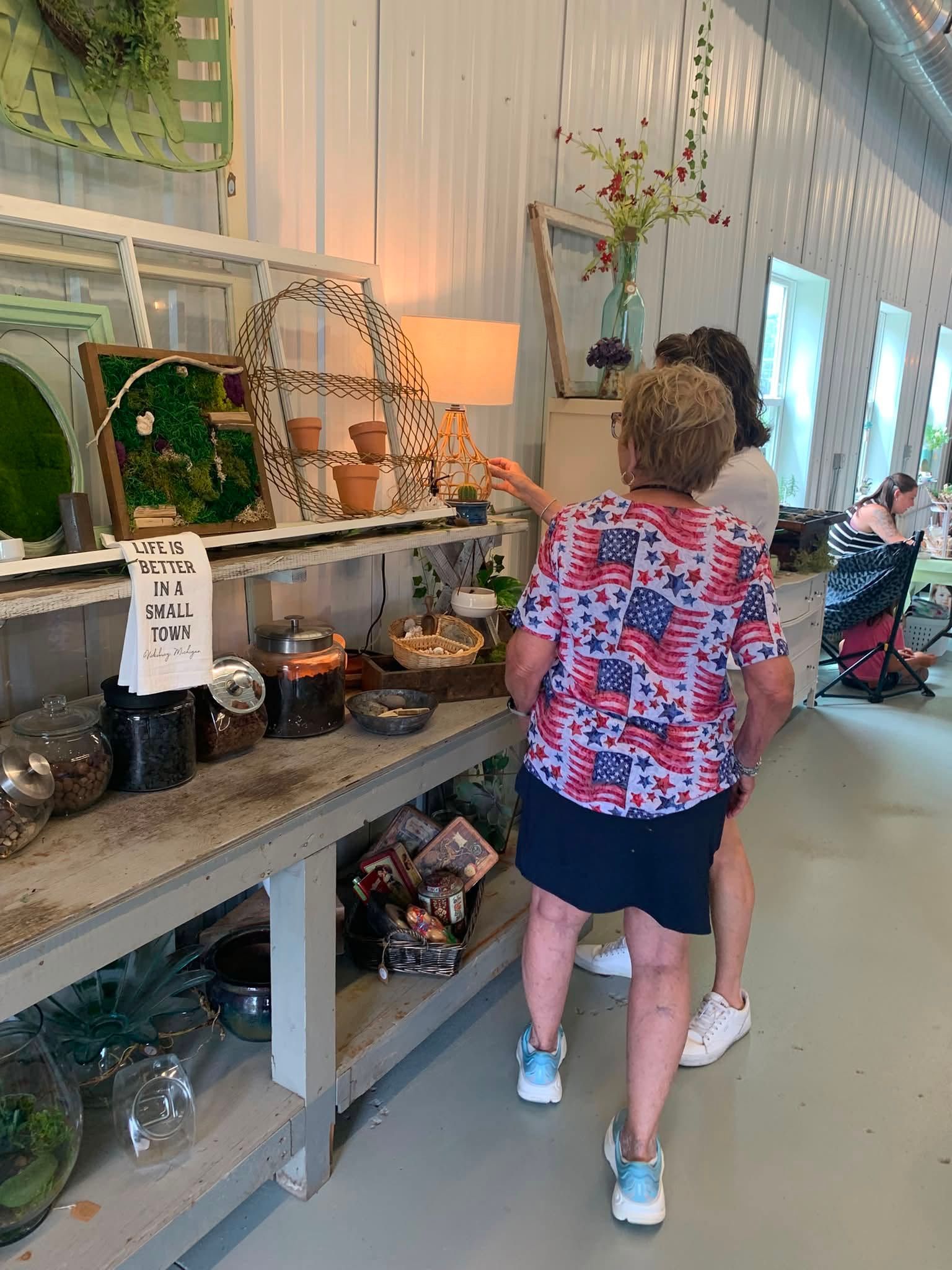 Person in red floral shirt browsing a gift display in a bright shop or gallery interior