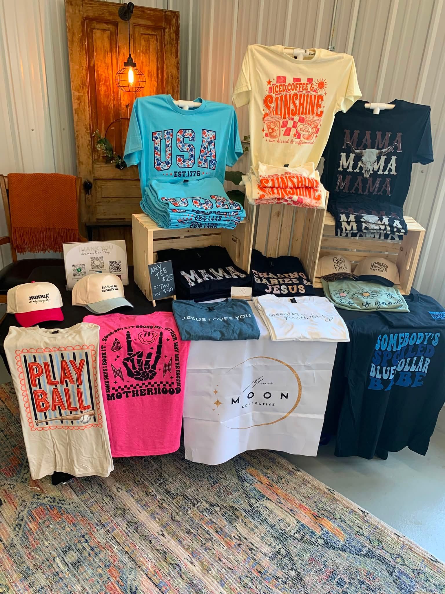 T-shirts and sweatshirts on display in a boutique, arranged on shelves and hanging against a rustic wooden backdrop.